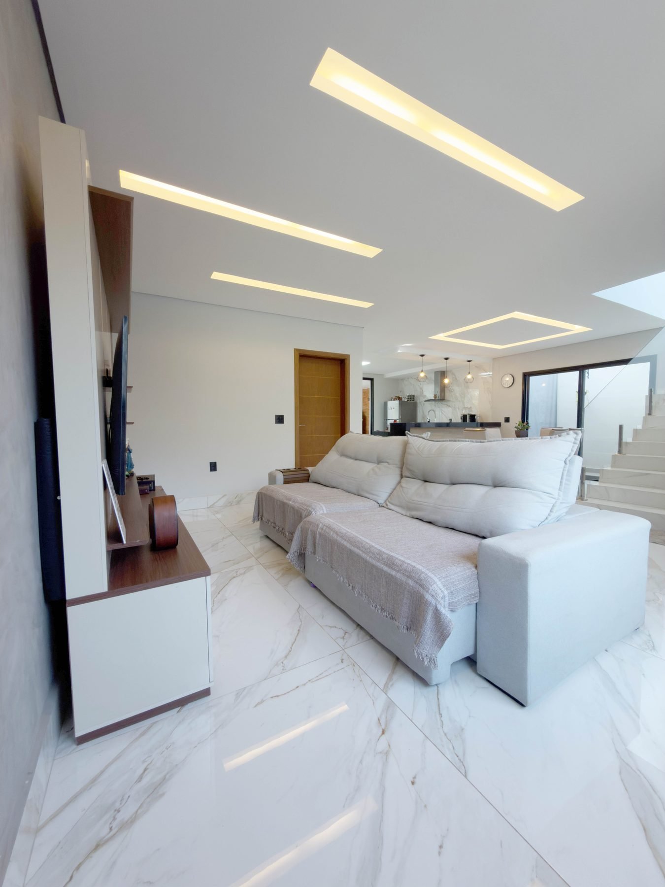 Sala de estar integrada, com porcelanato marmorizado e iluminação embutida no forro